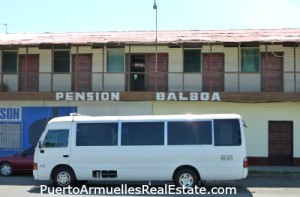 white bus passing in front of brown & yellow rundown hotel