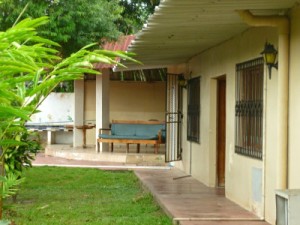 Green grass, cement walk way, building and couch in distance